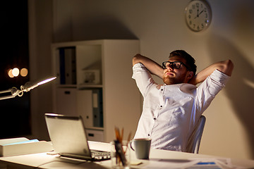 Image showing man with laptop stretching at night office