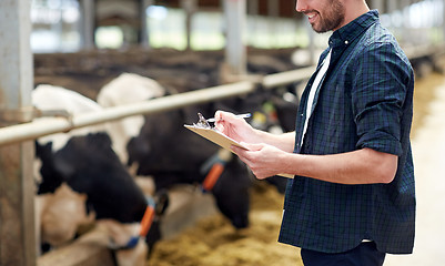 Image showing farmer with clipboard and cows in cowshed on farm