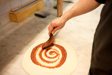 Image showing cook applying tomato sauce to pizza at pizzeria