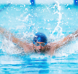 Image showing dynamic and fit swimmer in cap breathing performing the butterfly stroke