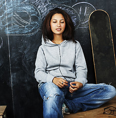 Image showing young cute teenage girl in classroom at blackboard seating on ta