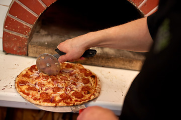 Image showing cook hands cutting pizza to pieces at pizzeria