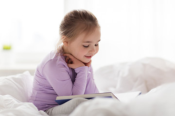 Image showing happy little girl reading book in bed at home