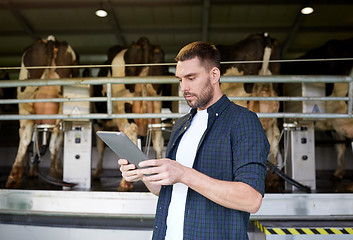 Image showing young man with tablet pc and cows on dairy farm