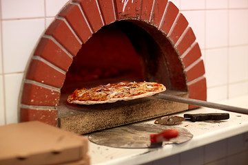 Image showing peel taking baked pizza out of oven at pizzeria