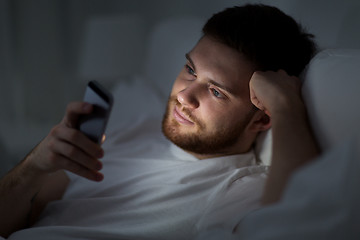 Image showing young man with smartphone in bed at night