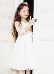 Image showing little cute girl at home, opening door well-dressed in white dre