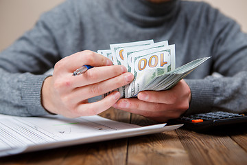 Image showing Caucasian hands counting dollar banknotes on dark wooden table