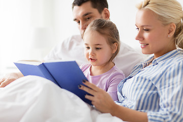 Image showing happy family reading book in bed at home