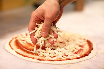 Image showing cook hand pouring cheese to pizza at pizzeria