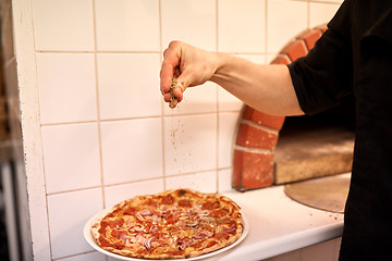 Image showing cook adding pepper to salami pizza at pizzeria