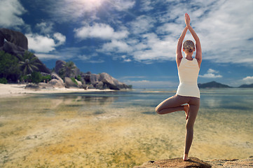 Image showing young woman making yoga tree pose over beach