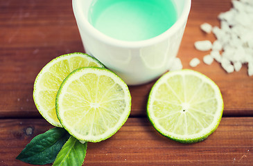 Image showing close up of body lotion in cup and limes on wood