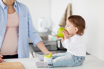 Image showing mother and baby eating green apple at home kitchen