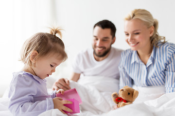 Image showing happy family with gift box in bed at home