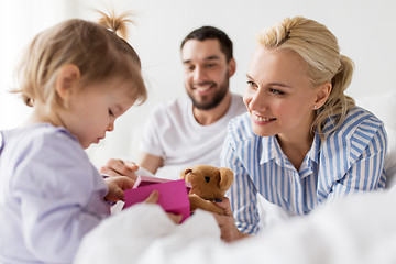 Image showing happy family with gift box in bed at home