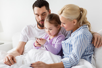 Image showing happy family with smartphone in bed at home