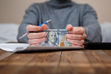 Image showing Caucasian hands counting dollar banknotes on dark wooden table