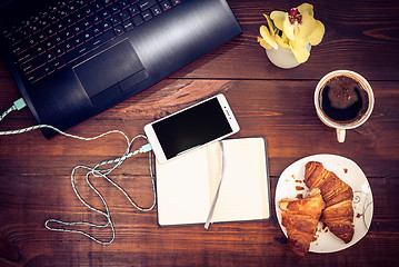 Image showing Workspace with laptop, smartphone, croissant, cofee on a wooden 