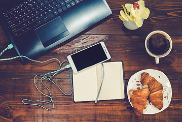 Image showing Workspace with laptop, smartphone, croissant, cofee on a wooden 