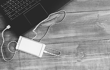 Image showing Workspace with laptop and charging blank smartphone on wooden de