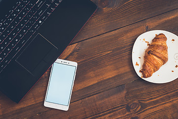 Image showing Workspace with laptop, smartphone and croissant on wooden desk