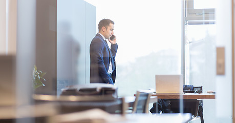 Image showing Businessman talking on a mobile phone while looking through window.