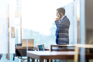 Image showing Businessman talking on a mobile phone while looking through window in NY