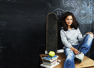 Image showing young cute teenage girl in classroom at blackboard seating on ta