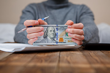 Image showing Caucasian hands counting dollar banknotes on dark wooden table