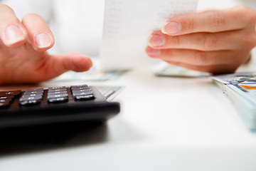 Image showing savings, finances, economy and home concept - close up of hands with calculator counting money and making notes at home