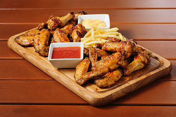 Image showing Big wooden board with grilled chicken winds