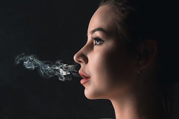 Image showing The face of vaping young woman at black studio