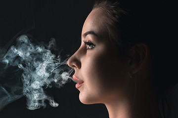 Image showing The face of vaping young woman at black studio