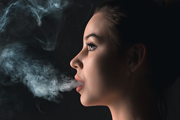 Image showing The face of vaping young woman at black studio