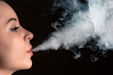 Image showing The face of vaping young woman at black studio