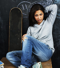 Image showing young cute teenage girl in classroom at blackboard seating on ta