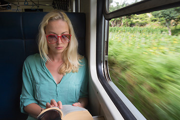 Image showing Blonde caucasian woman reading book on train by the window.