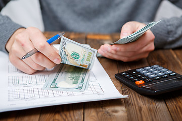 Image showing Caucasian hands counting dollar banknotes on dark wooden table