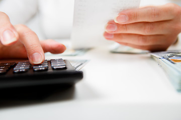 Image showing savings, finances, economy and home concept - close up of hands with calculator counting money and making notes at home