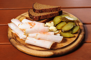 Image showing Wooden plate with smoked bacon, pickles and rye bread