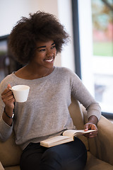 Image showing black woman reading book  in front of fireplace