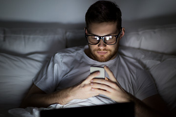 Image showing man with laptop and smartphone at night in bed