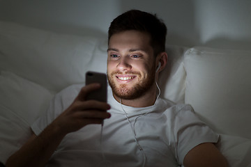 Image showing man with smartphone and earphones in bed at night