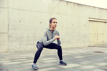 Image showing happy woman doing squats and exercising outdoors