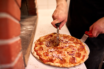 Image showing cook hands cutting pizza to pieces at pizzeria