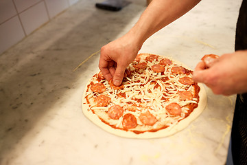 Image showing cook hands adding salami to pizza at pizzeria