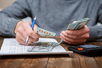 Image showing Caucasian hands counting dollar banknotes on dark wooden table