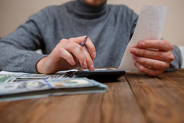 Image showing savings, finances, economy and home concept - close up of hands with calculator counting money and making notes at home