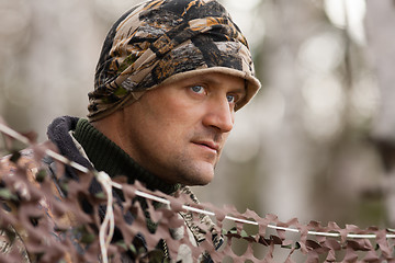 Image showing hunter looks out from behind camouflage netting